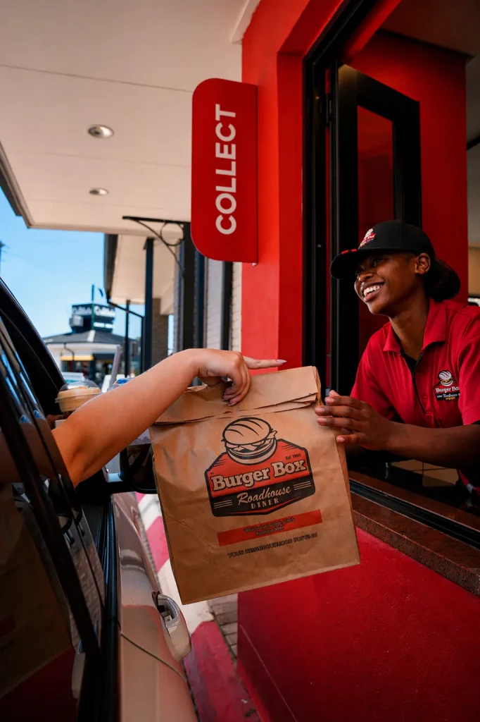 Burger Box staff member handing a takeaway order bag to a customer at the drive-thru window