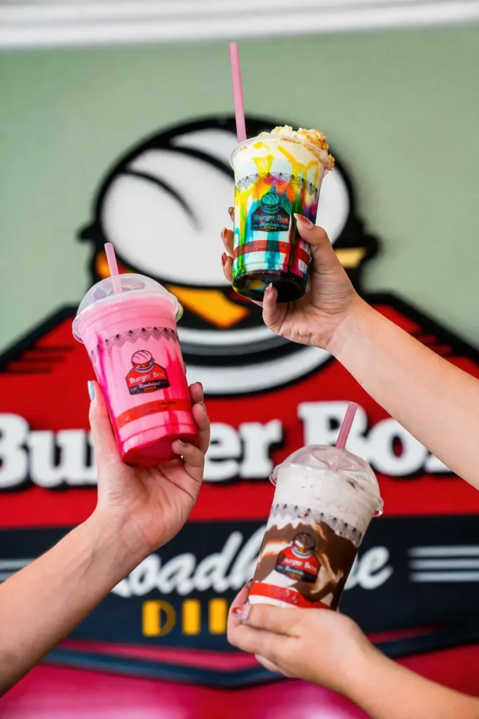 Three Burger Box milkshakes held up in front of the Burger Box Roadhouse sign